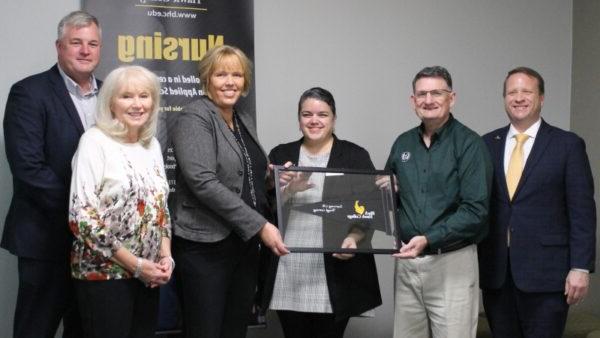 6 people standing in front of nursing banner with framed Black Hawk College pennant