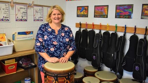 music teacher behind a drum with drums 和 ukuleles behind her